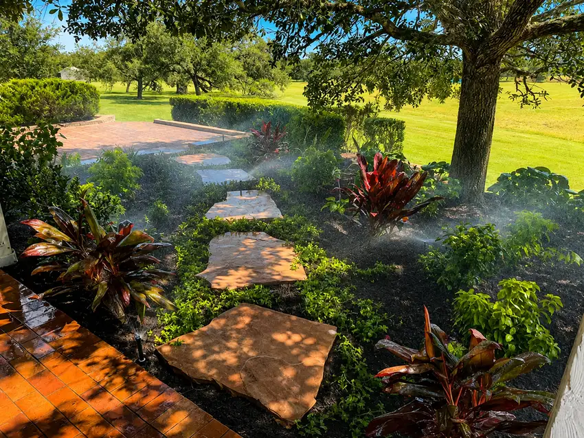 Flagstone stepping stones through a planted bed with irrigation running — Landscape Design & Maintenance